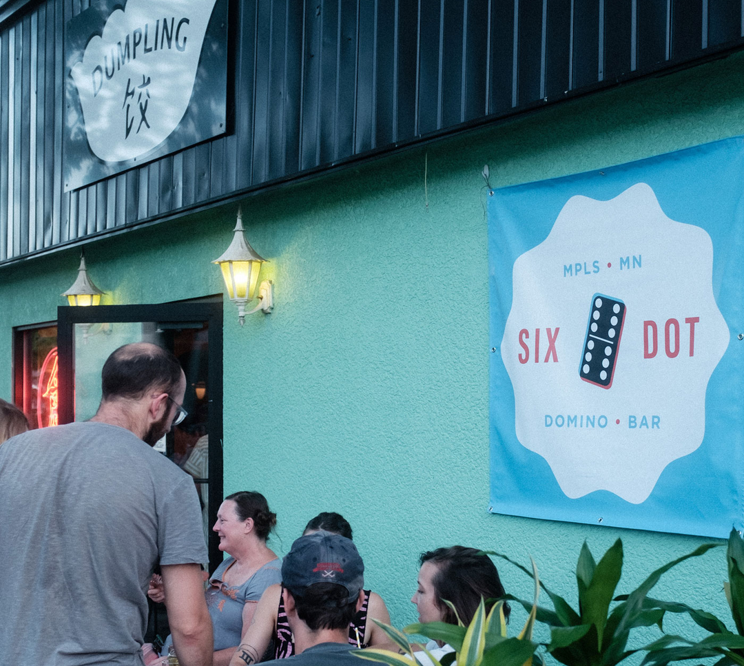 Banner with Six Dot logo hanging on a wall outside of a restaurant.